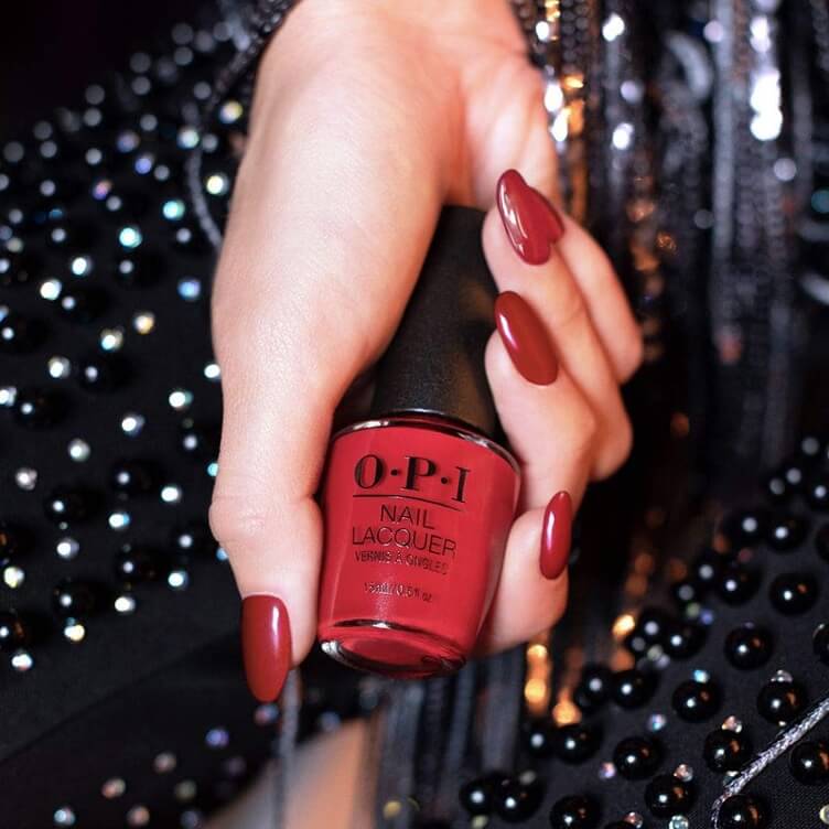 Hand holding a bottle of OPI Nail Lacquer in a deep red shade