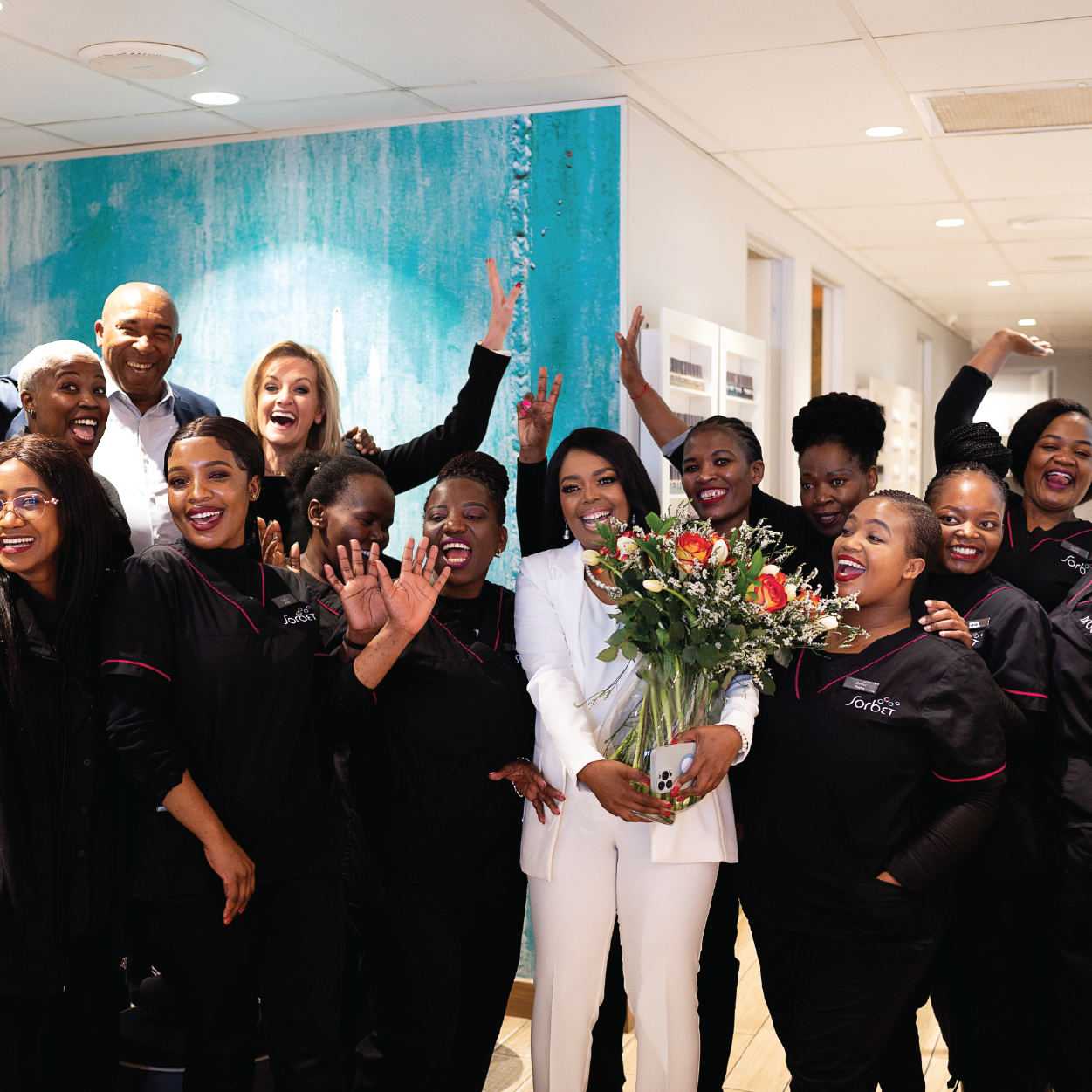 Celebration group photo of diverse beauty salon team with smiling staff, bouquet of flowers