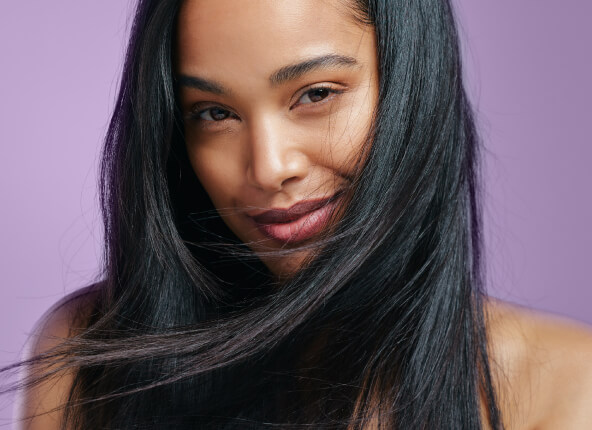 Woman with long, smooth black hair posing against a purple background, showcasing healthy shine and sleek styling.