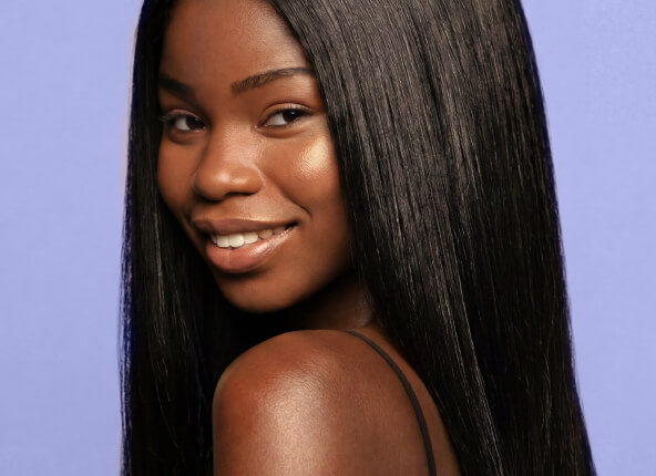 Portrait of a smiling Black woman with long straight black hair against a purple background.