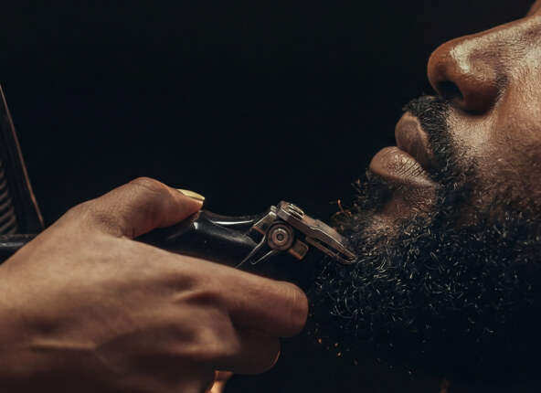 Close-up of a man using an electric beard trimmer to shape his facial hair.