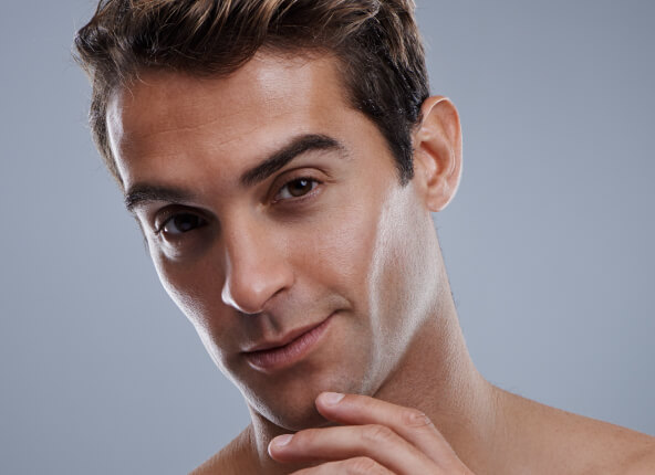 Close-up of a young man with dark hair touching his chin, looking thoughtfully at the camera