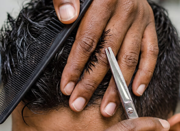 Barber trims client’s dark hair with scissors while holding a comb nearby.